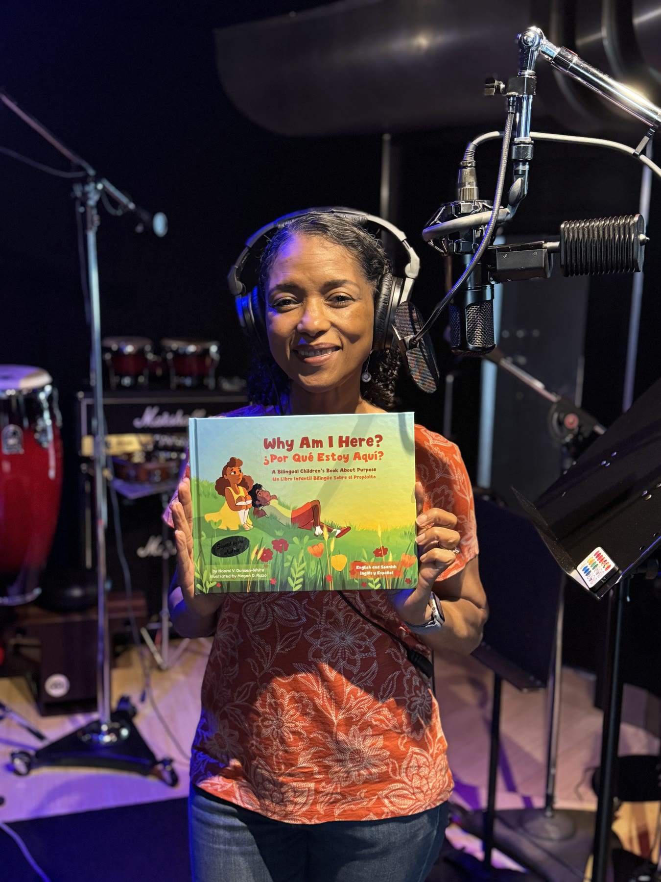 Naomi in the recording studio holding the Why Am I Here? bilingual book beside a microphone