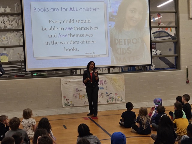 Naomi V. Dunsen-White speaking to students beneath a Books are for ALL children presentation