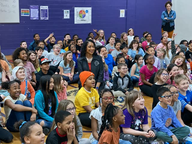 Naomi V. Dunsen-White seated among a large group of students during a school visit
