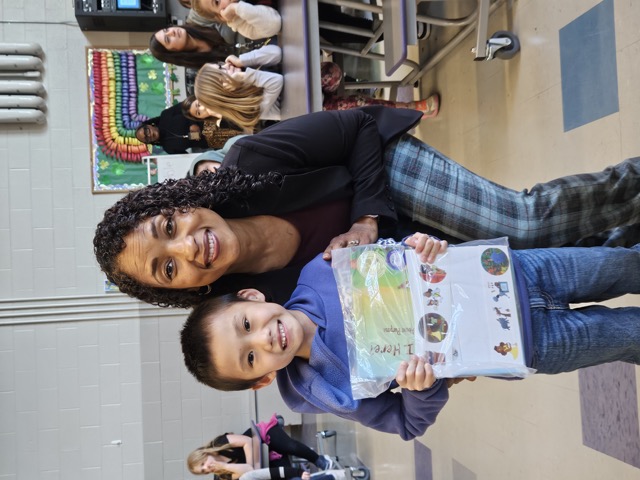 Naomi V. Dunsen-White kneeling beside a smiling young reader holding a book
