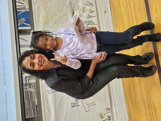 Naomi V. Dunsen-White smiling with a young reader holding a book after a school visit