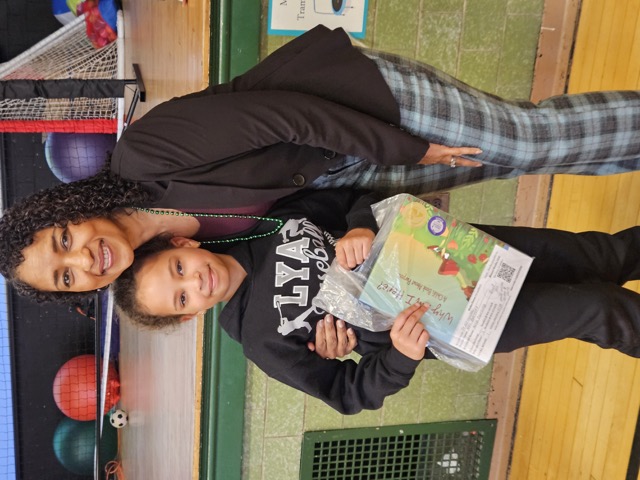 Naomi V. Dunsen-White smiling with a young reader holding Why Am I Here?