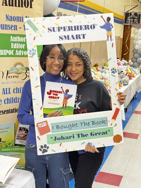 Naomi V. Dunsen-White and a guest posing with Johari the Great in a Superhero Smart photo frame