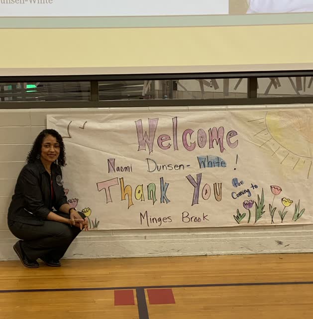 Naomi V. Dunsen-White beside a handmade school welcome and thank-you banner